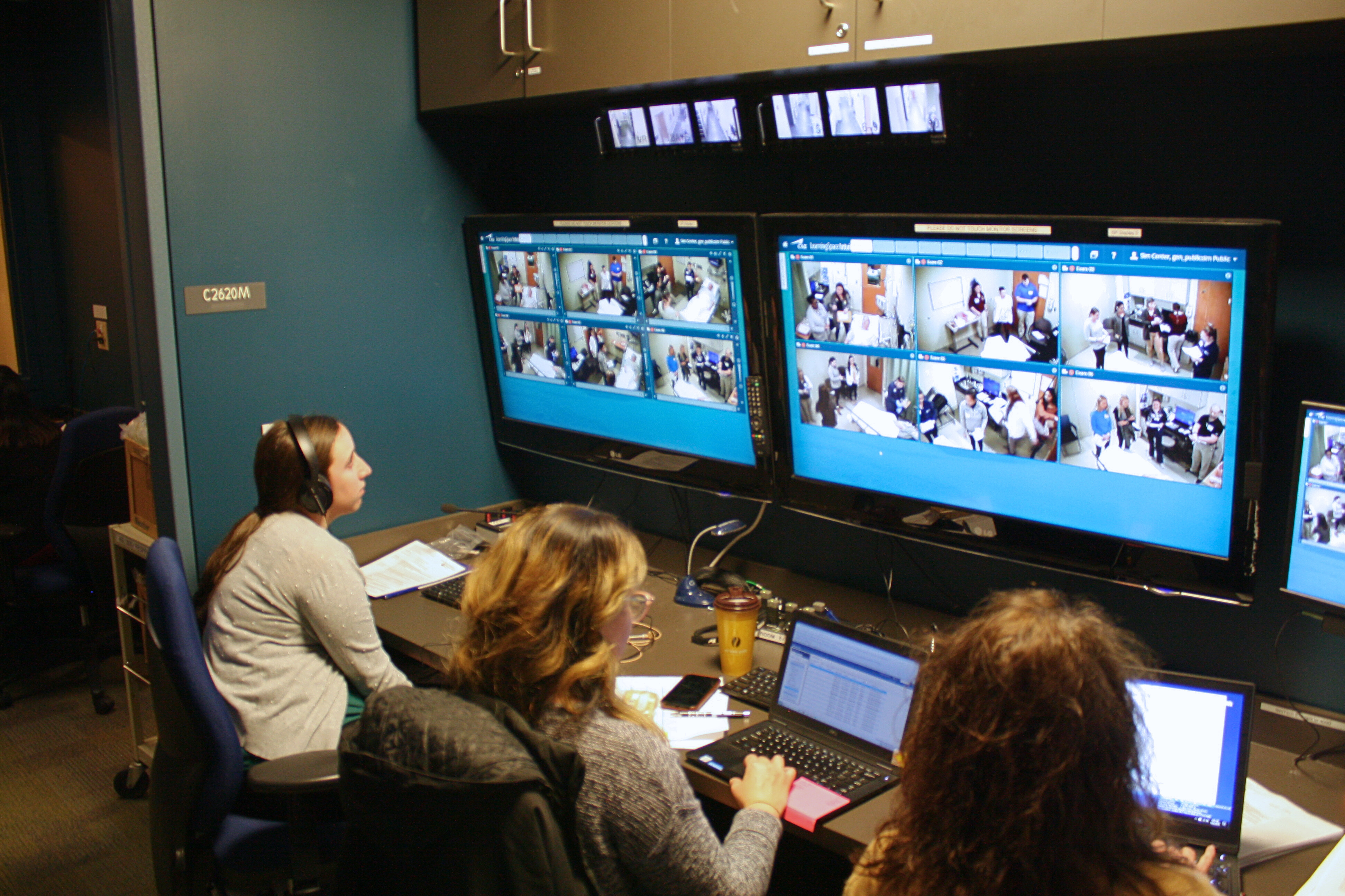 Simulation control room with staff monitoring multiple live training scenarios on large screens.