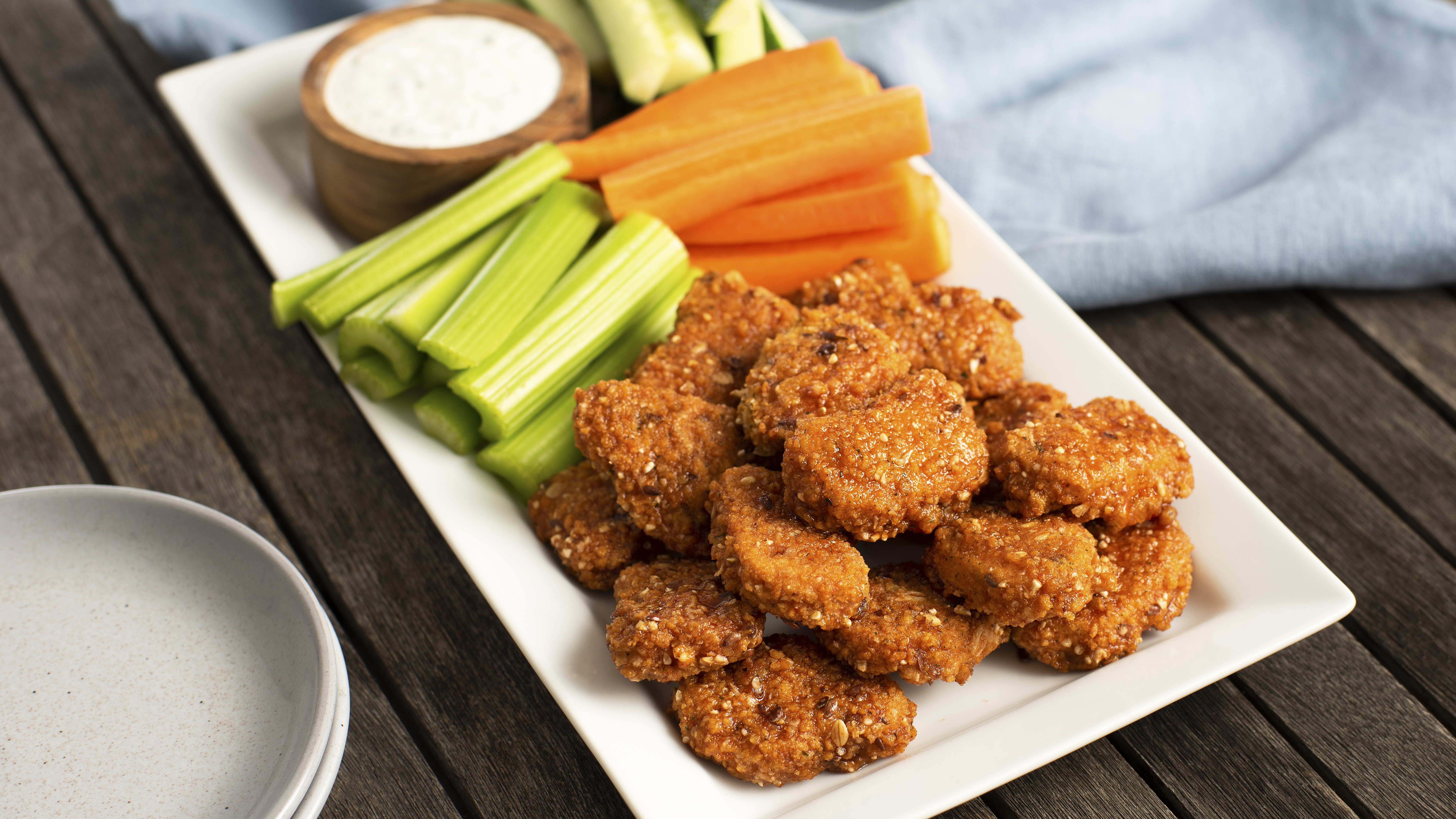 Quorn Vegan Meatless Buffalo Dippers served on a white rectilinear plate with carrot and celery sticks and vegan blue cheese dip on the side.