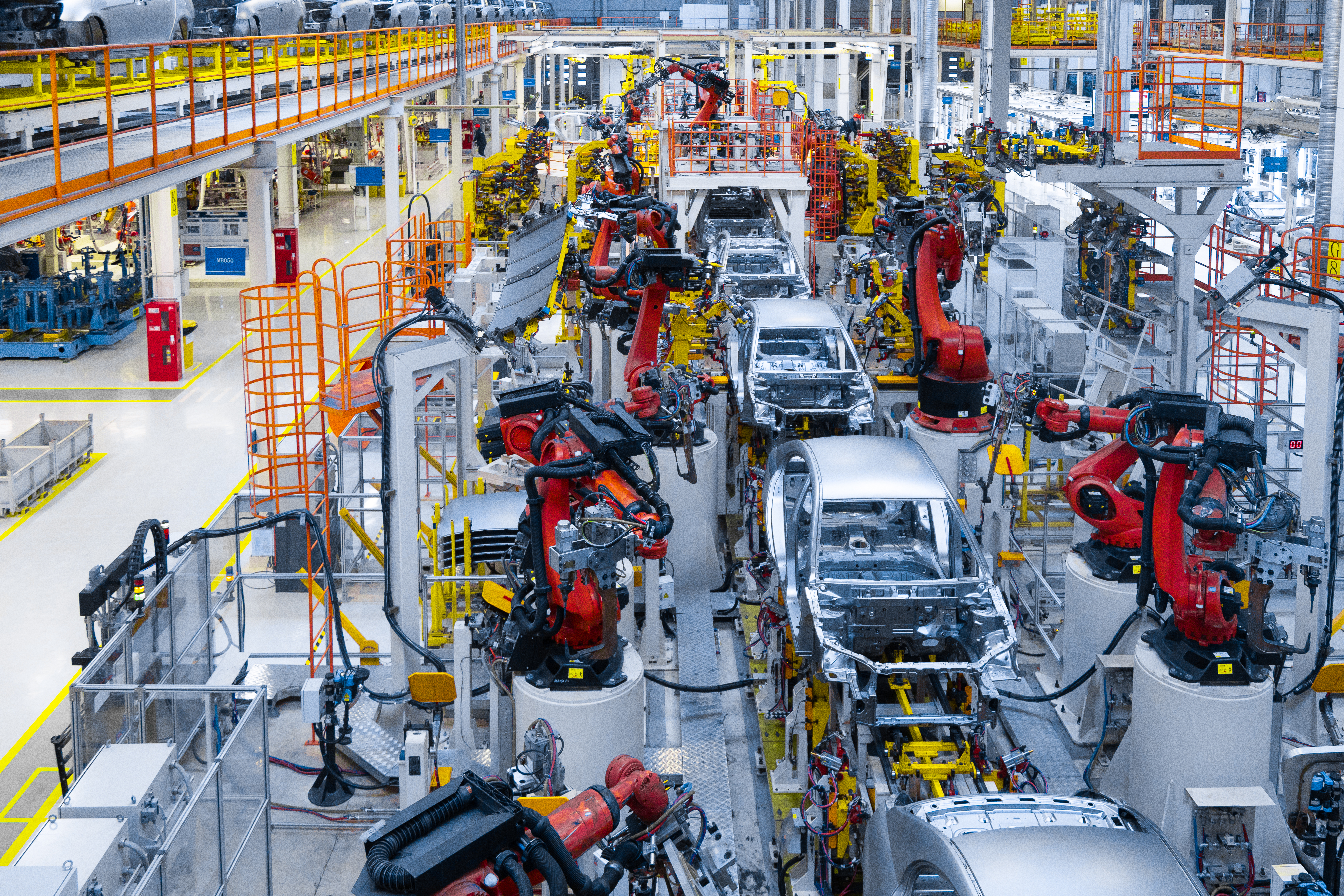 An automotive factory is filled with robotic arms assembling cars on a production line.  