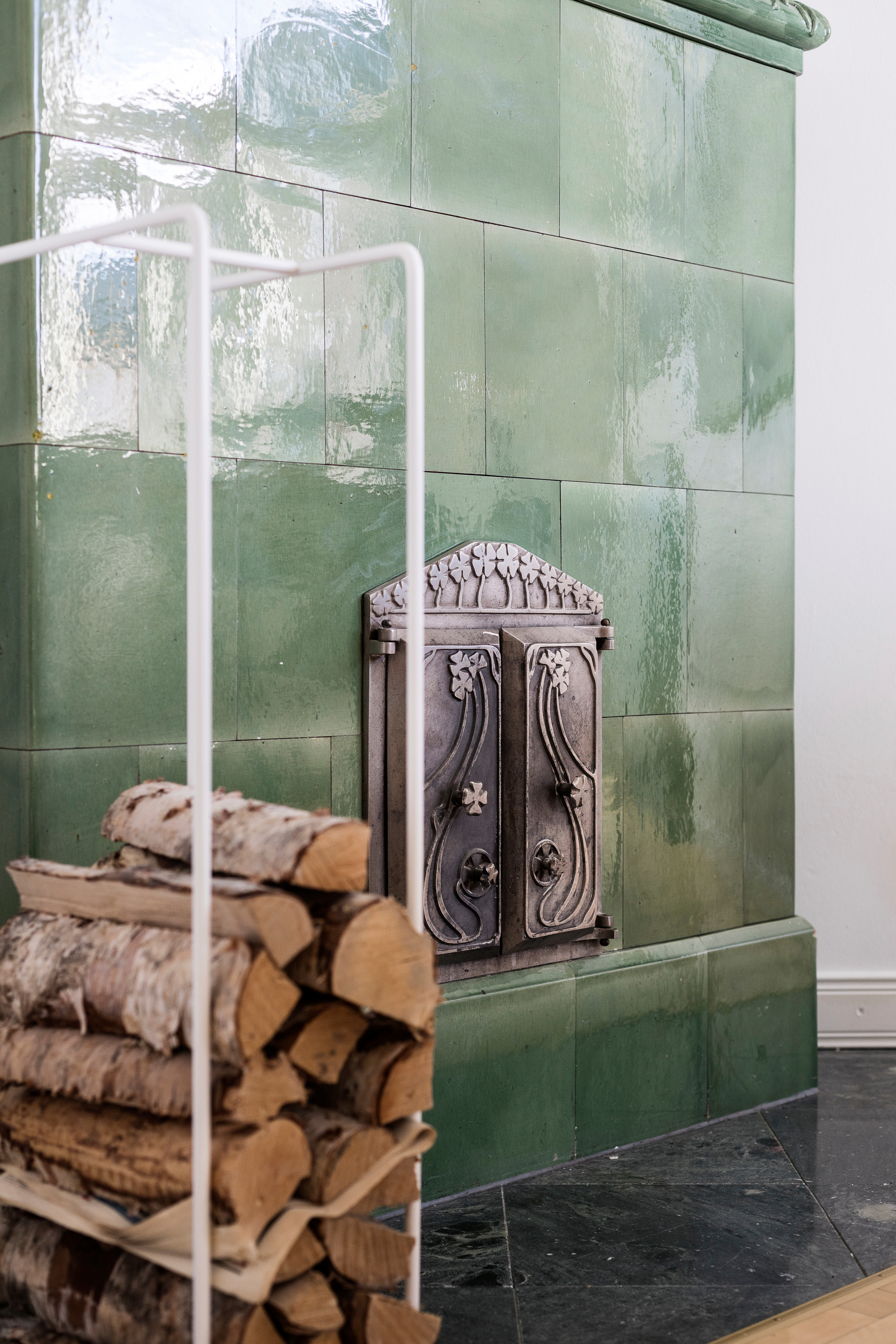 ornate stove doors on a green tile stove, with firewood nearby