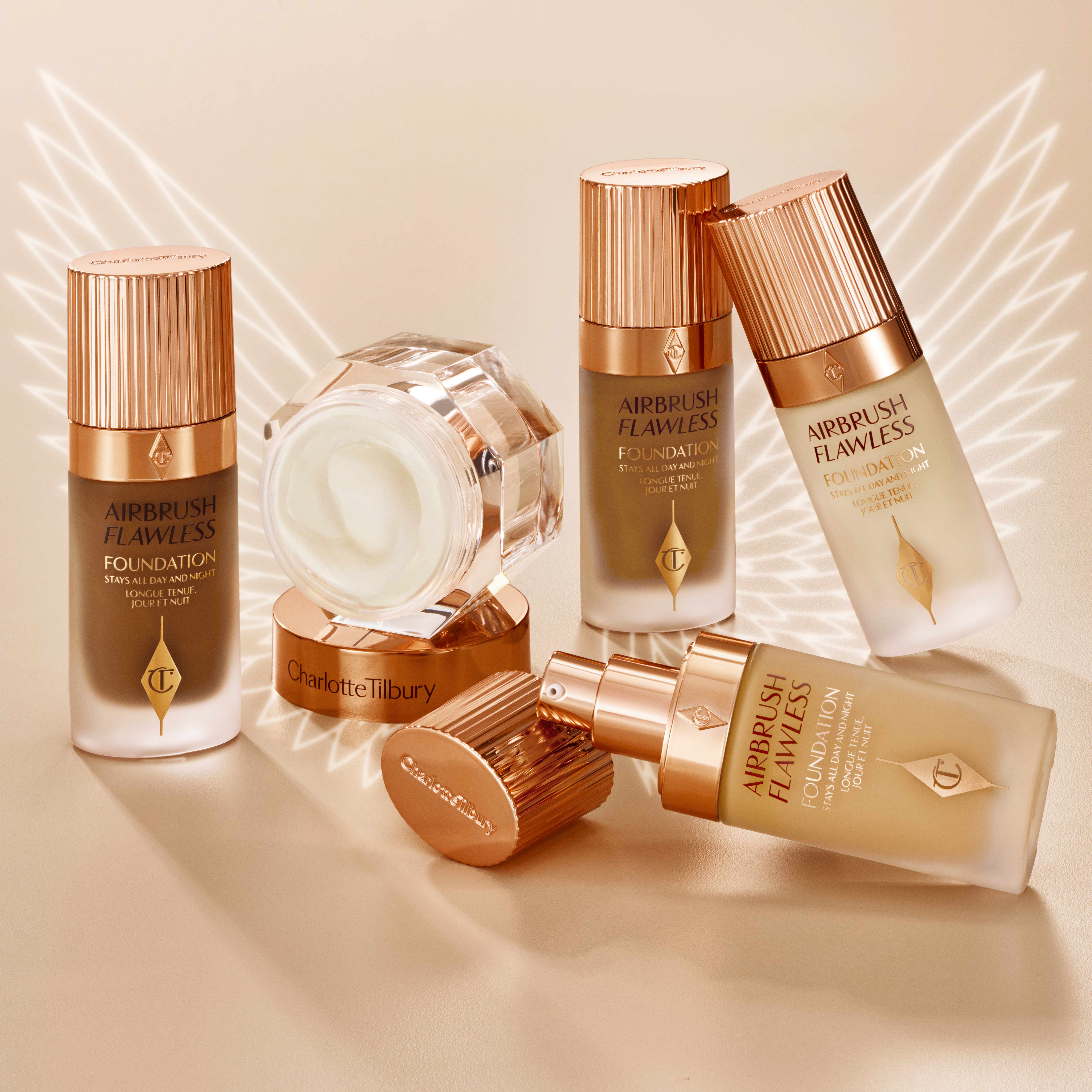 Thick, pearly-white cream in an open glass jar with its rose-gold-coloured lid next to it along with a collection of foundation in different shades, in frosted glass bottles with gold-coloured lids.