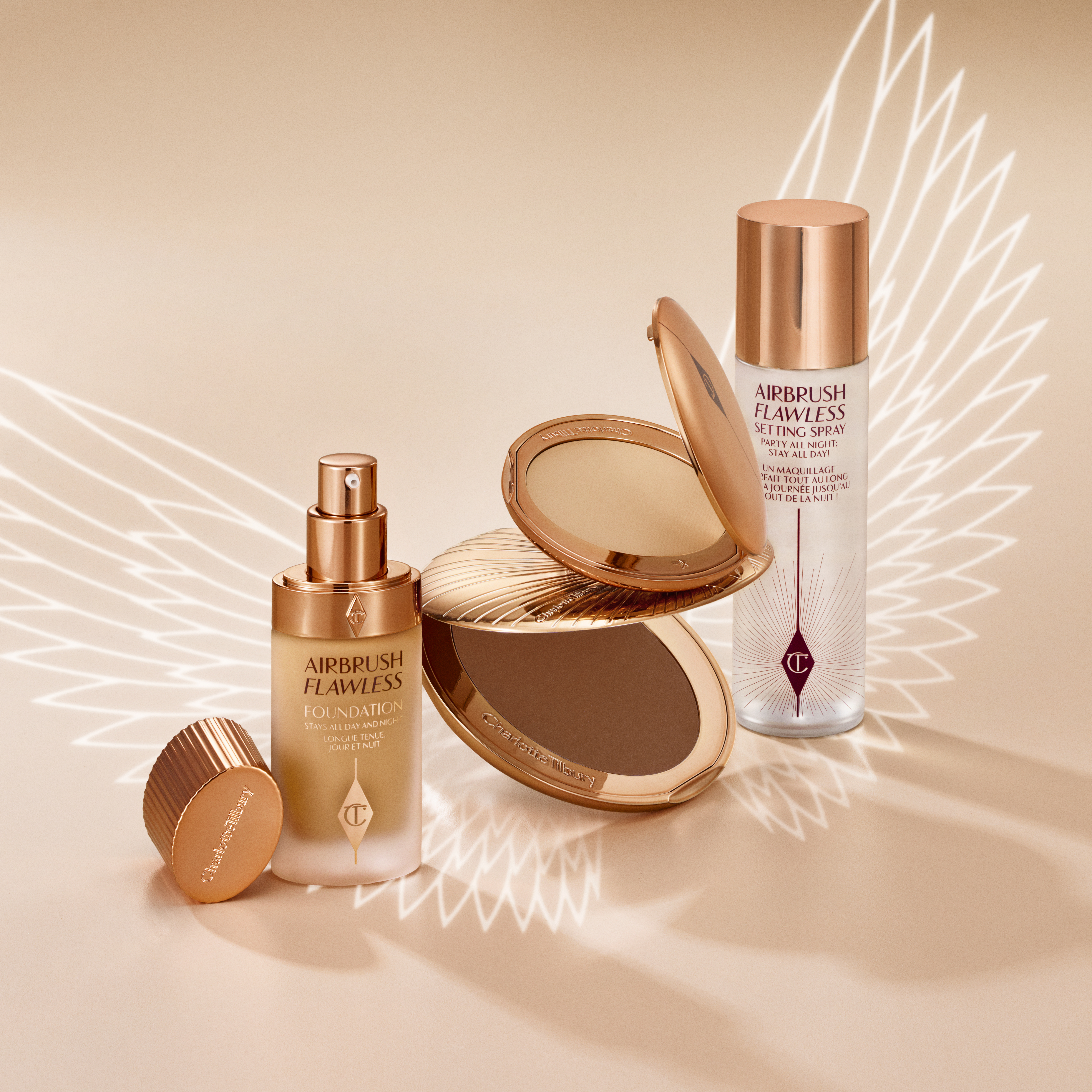 Banner with a collection of makeup that includes a setting spray, setting powder compact, foundation in a frosted glass bottle with a pump dispenser, and a bronzer compact, all in sleek, gold-coloured packaging