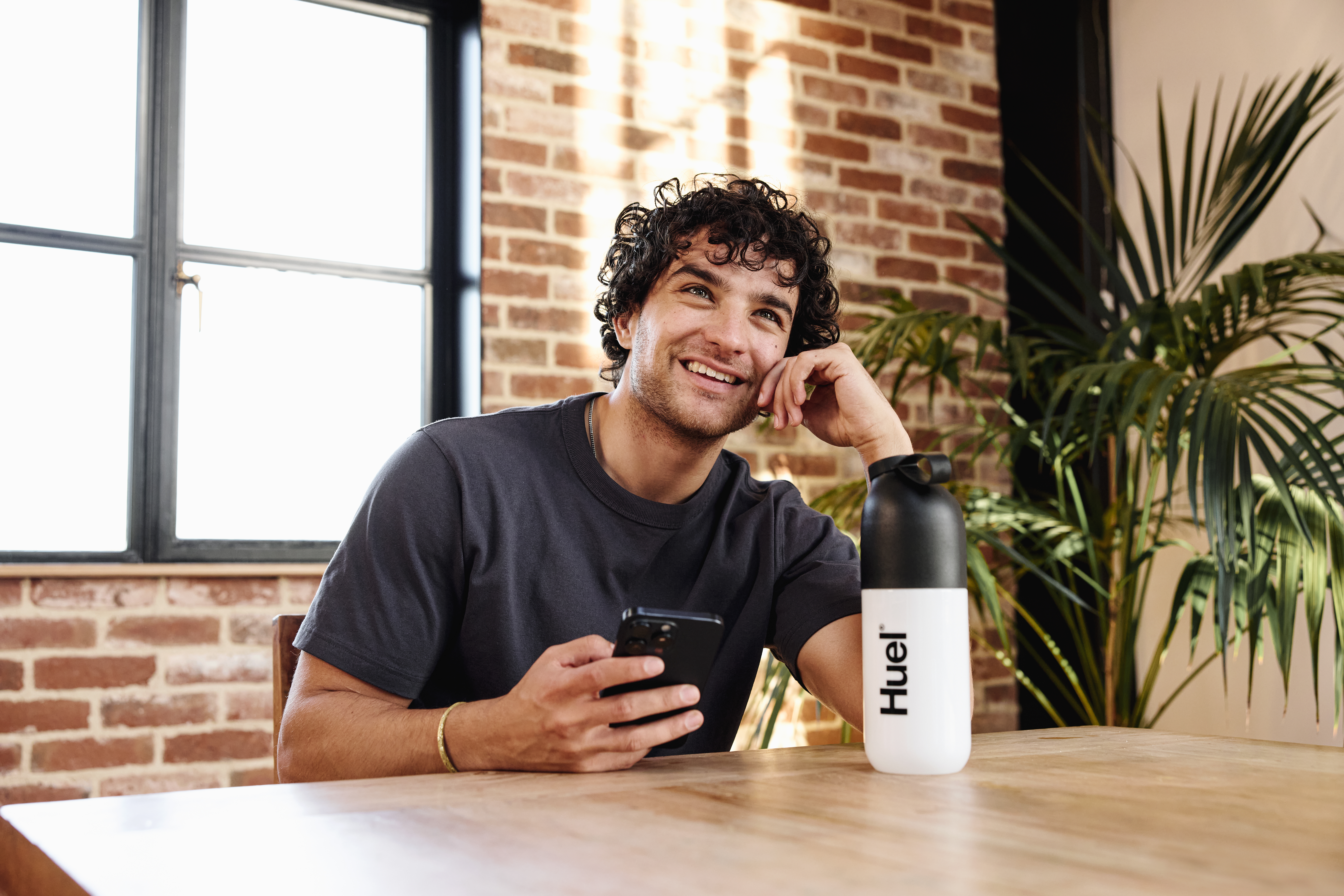 man sat at a table on his phone with a huel shaker on the table in front of him